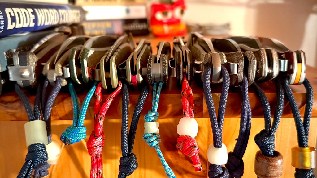 A collection of knives with lanyards and lanyard beads on top of a bookcase.