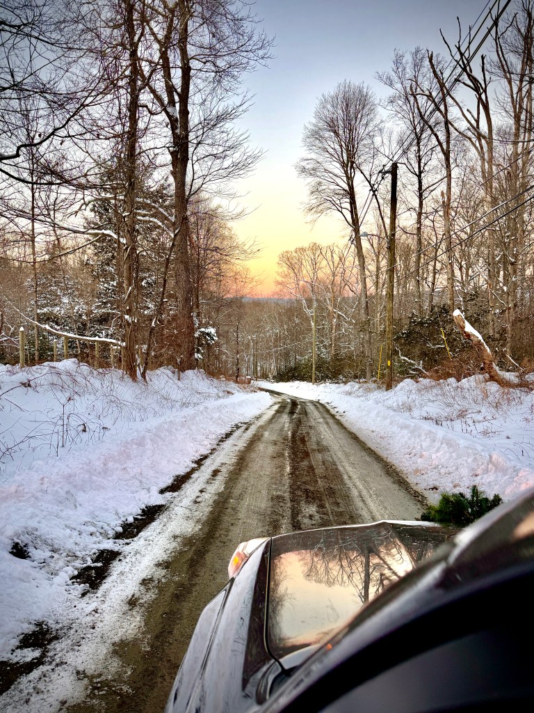 Driving down a snowy road during sunset.